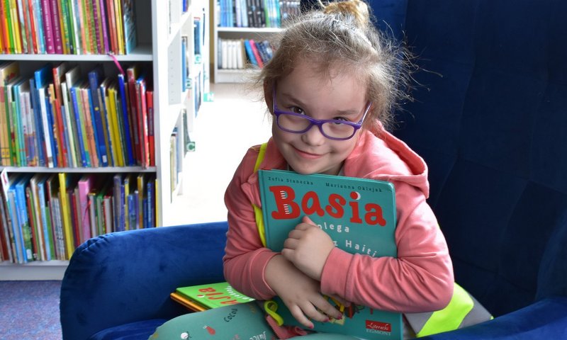 Na zdjęciu dziewczynka z książką w bibliotece
