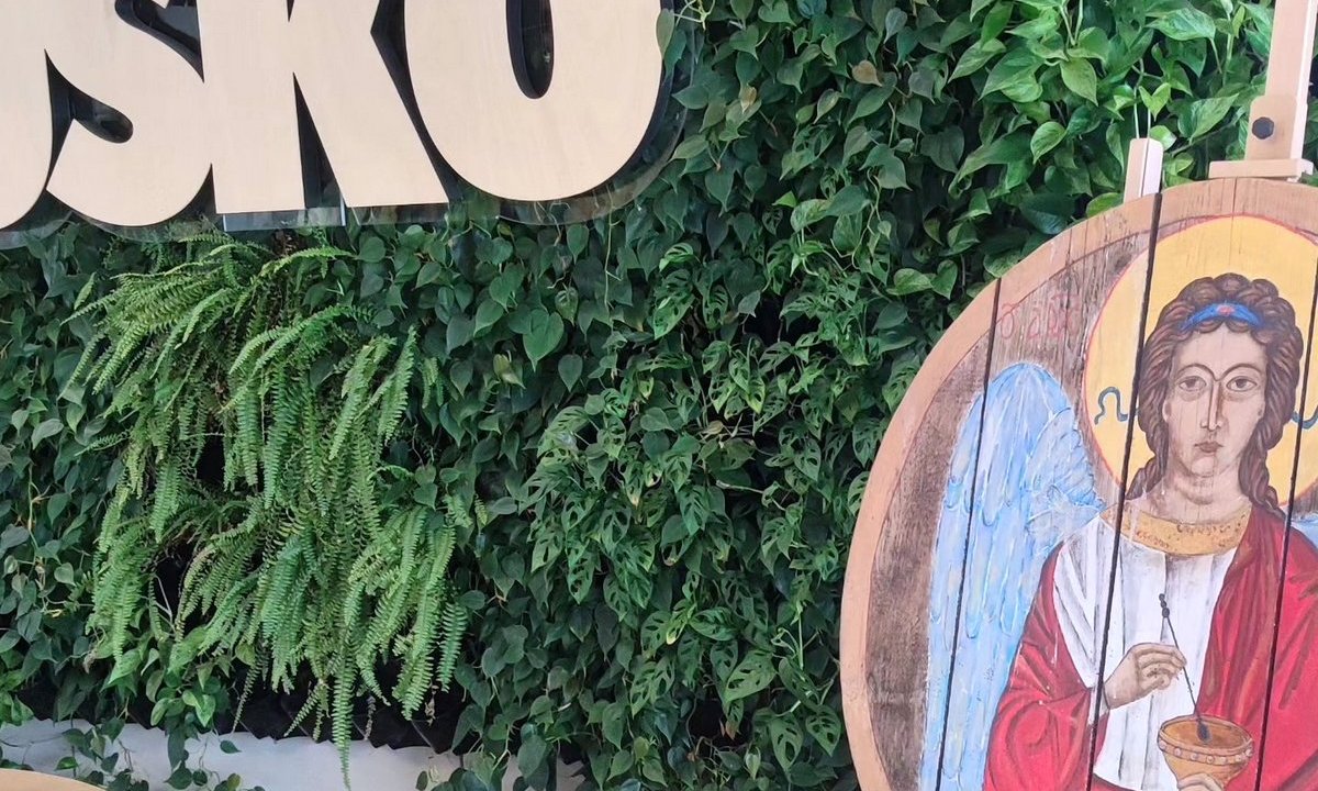 fragment wystawy Aniołowo w domu zdrojowym, praca plastyczna  przedstawiająca anioła nawiązująca do ikony, namalowana na drewnie, w tle zielona ściana roślin i napis Busko