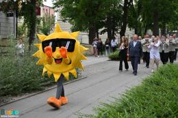 Na zdjęciu korowód festiwalowy idący aleją Mickiewicza prowadzony przez osobę w stroju maskotyki miejskiej - słoneczka
