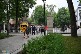 Korowód wkraczający do parku Zdrojowego prowadzony przez osobę w stroju maskotki miejskiej Słoneczka 